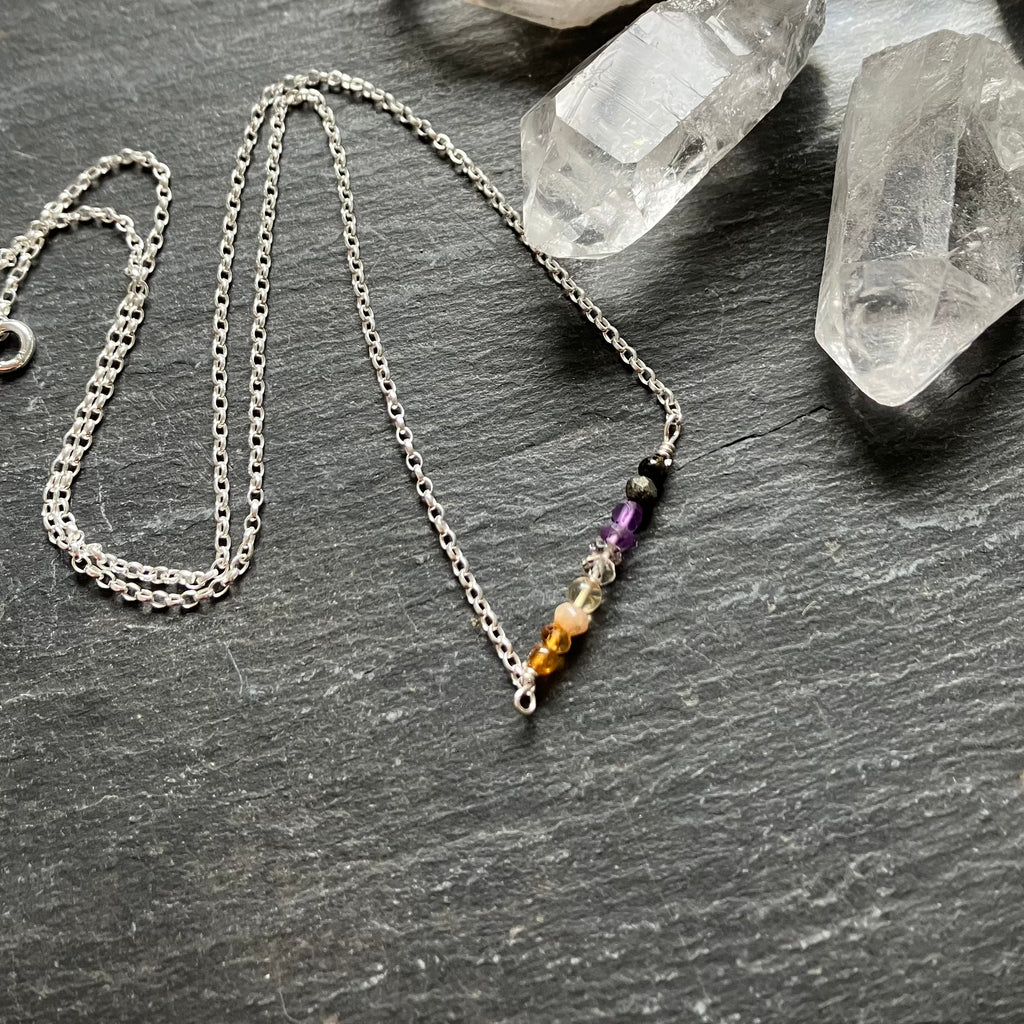 Silver necklace with colorful beads on a dark surface with crystals in the background
