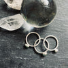 Three silver rings with small stones on a dark surface with crystal rocks.