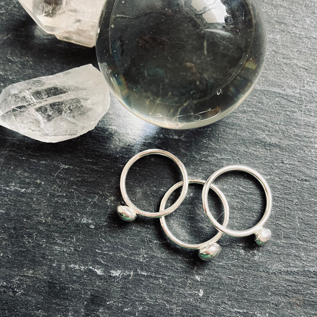 Three silver rings with small stones on a dark surface with crystal rocks.