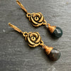 Pair of gold rose-shaped earrings with black beads on a dark surface