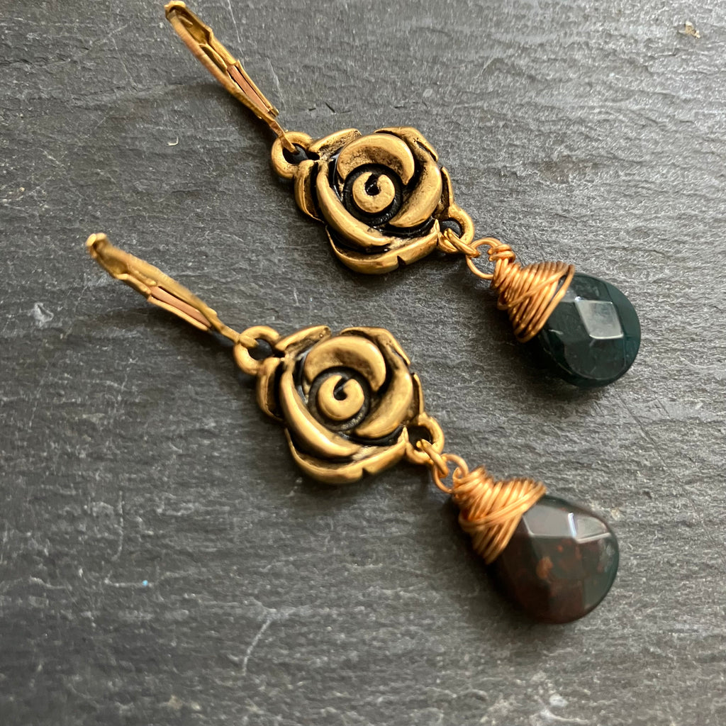 Pair of gold rose-shaped earrings with black beads on a dark surface
