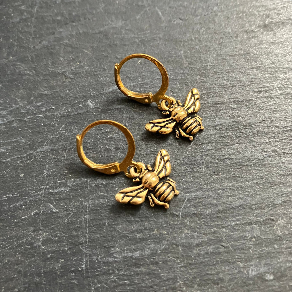 Gold bee earrings on a gray surface