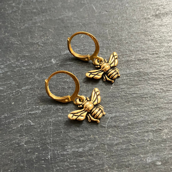 Gold bee earrings on a gray surface